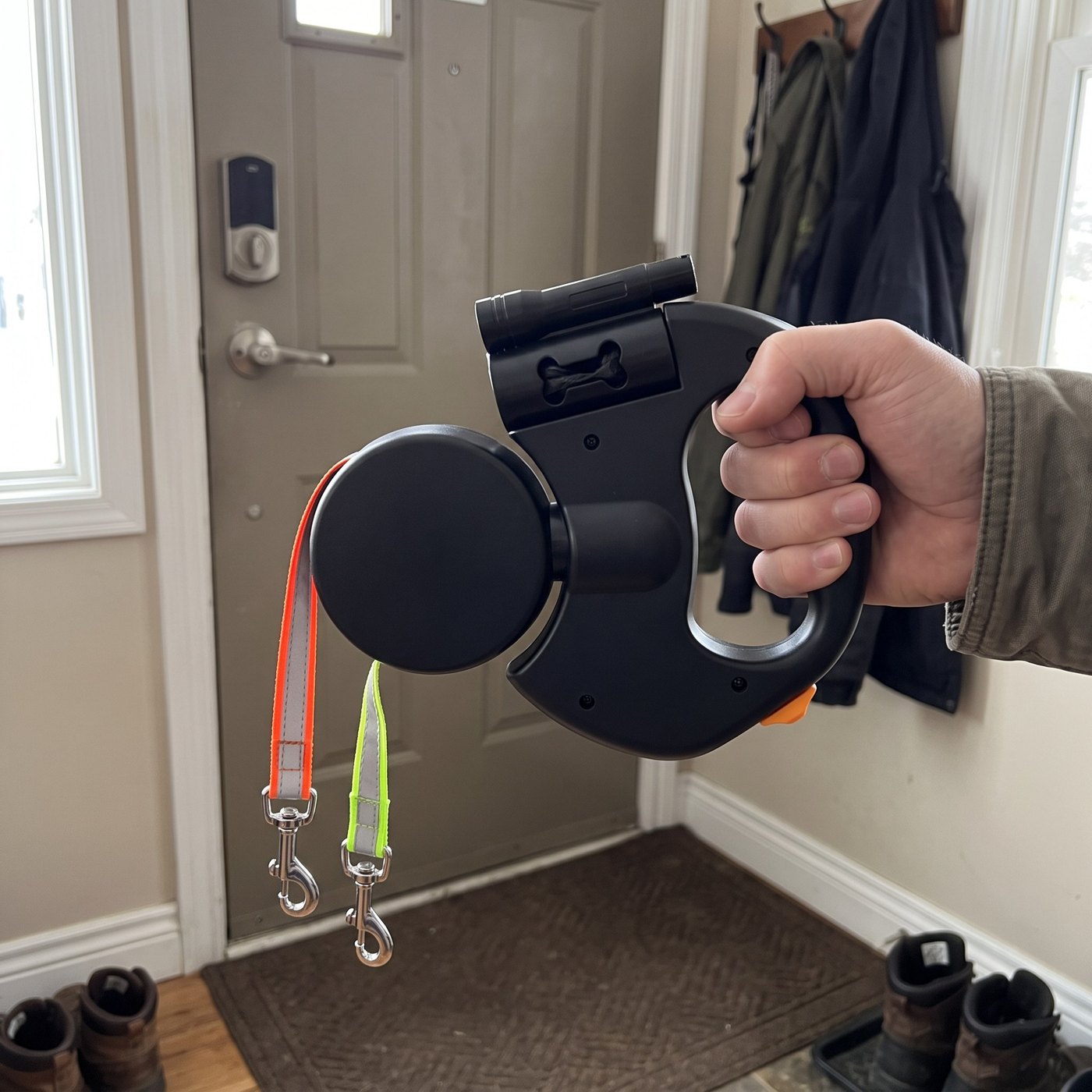 Candid close-up of leash hanging from adult hand by a front door, short hooks vi